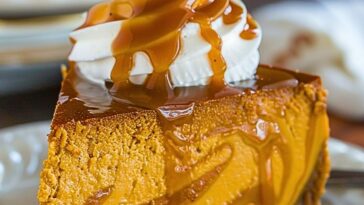 Slice of Pumpkin Caramel Swirl Cheesecake topped with whipped cream and caramel drizzle on a white plate